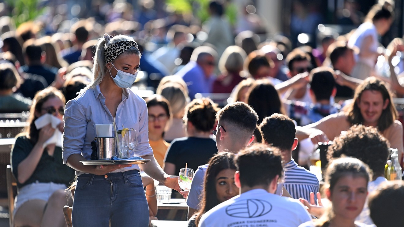 戴着防护面罩的女服务员在伦敦市中心苏活区的户外餐桌上为顾客带来饮料。英国政府部长们指责整个夏天人们都在放松对冠状病毒的限制。（图源：华尔街日报）.jpg